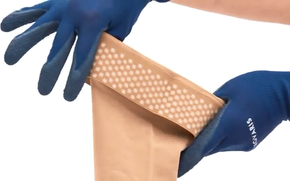 На фото - руки в перчатках держат антиварикозный чулок с силиконовыми вставками на резинке